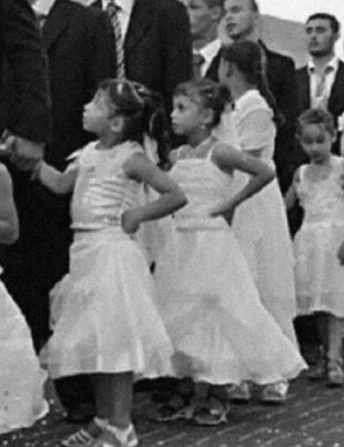 A line of young girls in white dresses standing beside adult men in black suits during a traditional ceremony in Iraq.